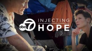Injecting Hope: Tackling Drug Overdose With Harm Reduction 3 A woman sitting and speaking to a homeless man living in a tent with the title, ABC 7: Injecting Hope.