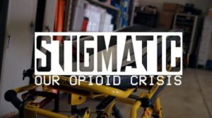 Stigmatic: Our Opioid Crisis 1 An EMS stretcher in a room with the title Stigmatic Our Opioid Crisis across the front.