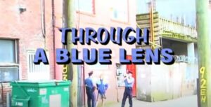 Two Vancouver police officers and an individual in an alleyway by a dumpster, standing and talking, with the title, Through A Blue Lens