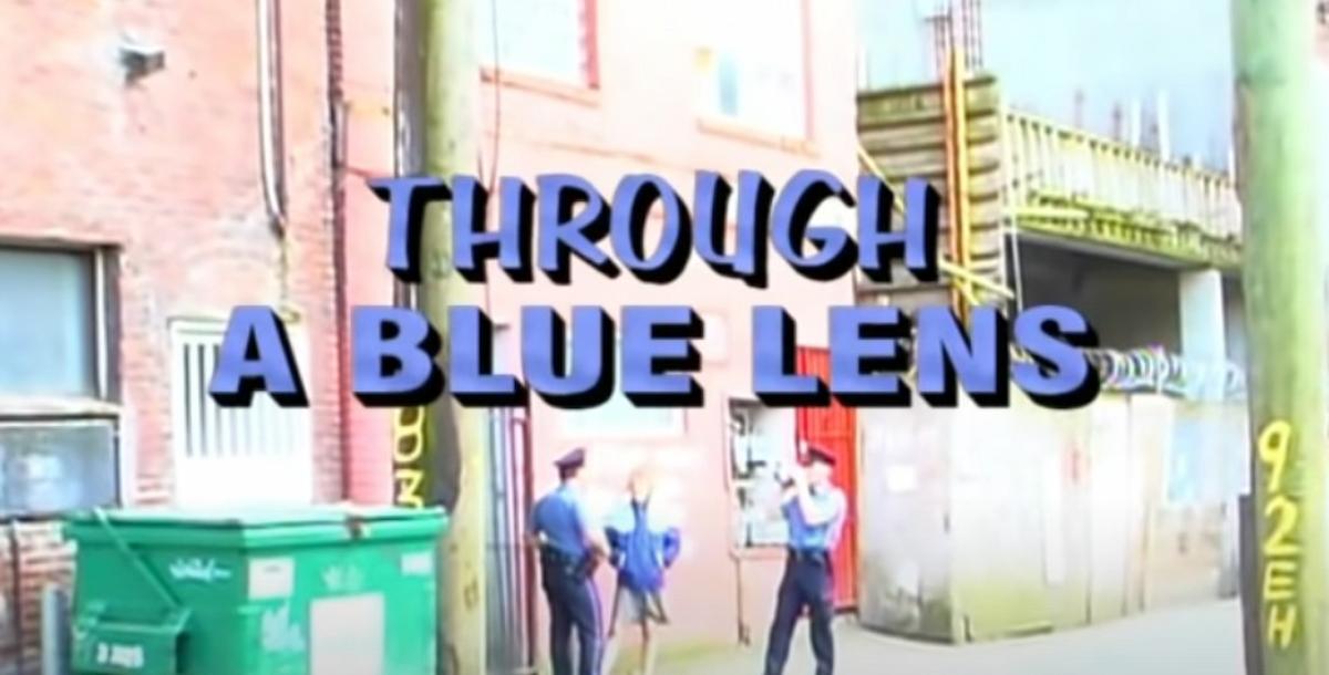 Two Vancouver police officers and an individual in an alleyway by a dumpster, standing and talking, with the title, Through A Blue Lens